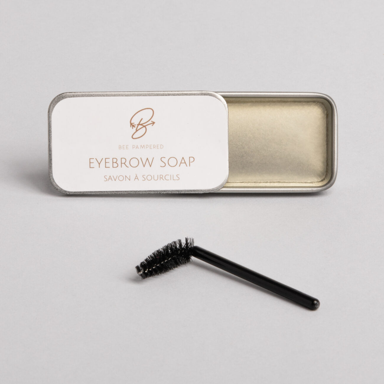 "Brow Styling Soap, clear gel in a small jar, designed to shape and hold brows in place for a polished, natural look. Rectangular tin with a white top