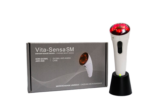 "White handle with red end on the Vita-Sensa SM facial stimulator, a handheld device with a sleek, ergonomic design. It features 10 small metal electrodes and 5 red light emitting diodes (LEDs) for microcurrent, light therapy, and vibromassage. The device comes with a gray transformer and base, a user guide, and a portable travel kit."